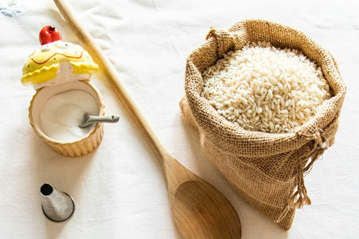 A sack of uncooked white rice beside a wooden spoon on a linen cloth